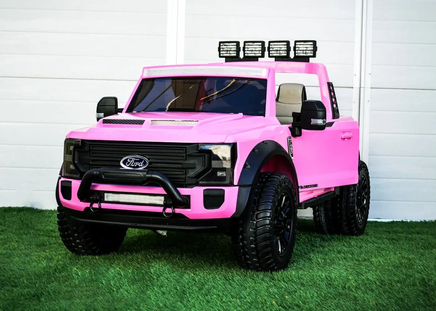 Kids ride on pink Ford Super Duty truck with remote and off-road tires on grass. Perfect for outdoor play.