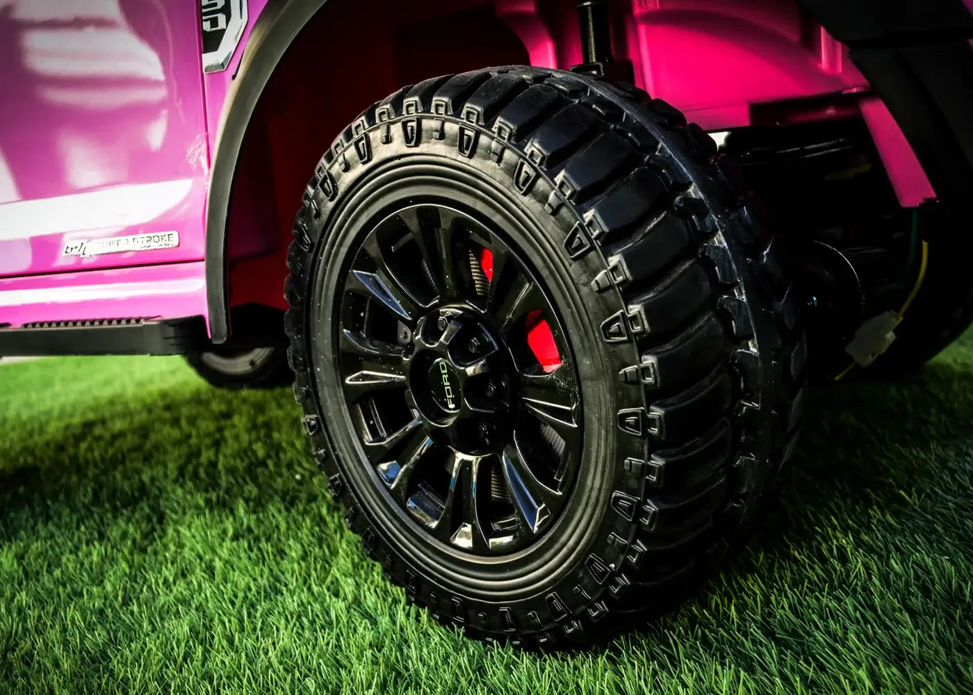 Close-up of the rugged black tire on a kids' ride-on Ford truck, featuring intricate tread patterns on green grass.