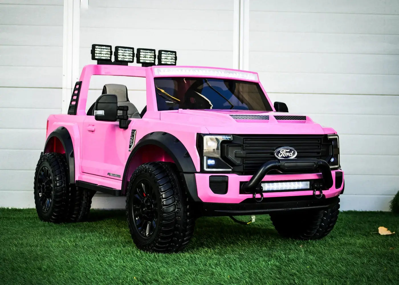 Pink kids ride-on Ford truck with remote, featuring stylish design and off-road tires on grass background.